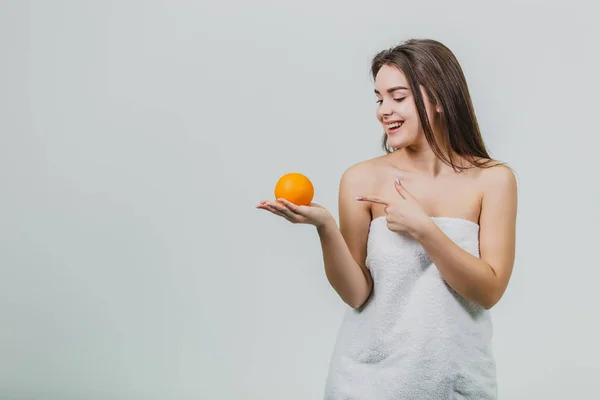 Retrato de una linda joven atractiva mujer de medio ojo sosteniendo una naranja en sus manos y mirando a una naranja, aislada sobre un fondo blanco . — Foto de Stock
