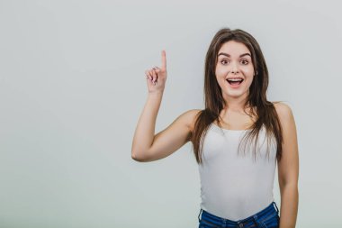 Güzel genç bir beyaz kız beyaz bir arka plan üzerinde durdu. Bu süre içinde beyaz bir T-shirt ve kot giymek. Onun parmağı ortaya çıktı, o onun geniş ağzını açık kameraya benziyor.