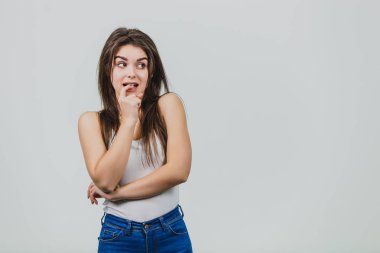 Genç güzel kız beyaz bir arka plan üzerinde ayakta. Bu sırasında o ağzına bir parmak koyar ve korkuyla yönde görünüyor. Güzel siyah uzun saçları var..