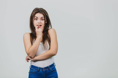 Genç güzel kız beyaz bir arka plan üzerinde ayakta. Bu sırasında onun ağzına bir parmak koyar ve sürpriz kamerada bakar. Güzel siyah uzun saçları var..