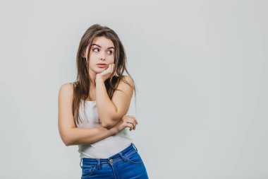 Beyaz bir arka plan üzerinde duran genç ve güzel bir kız. Kız beyaz bir gömlek giymiş. Güzel siyah uzun saçları var. Düşünme sonra çene altından elini koymuş. Tarafına bak.