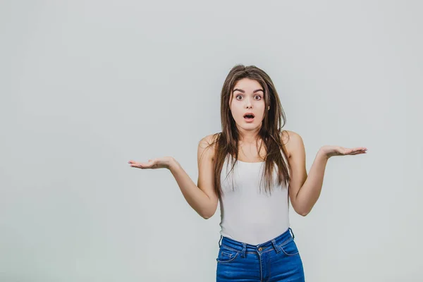 Une jeune belle fille se tient sur un fond gris tandis que vêtue de jeans bleus et d'un T-shirt blanc . — Photo