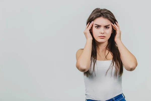 A young beautiful girl stands on a gray background while dressed in blue jeans and a white T-shirt. — Stock Photo, Image