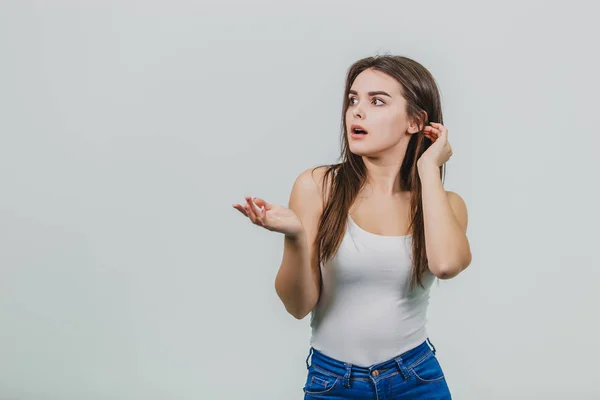 Primo piano di una bella ragazza in piedi su uno sfondo bianco. La ragazza è vestita con una camicia bianca e una maglia blu. Ha bei capelli lunghi neri. Sorpreso guardando in direzione di — Foto Stock