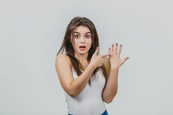 Chica joven es bastante caucásica de pie en un fondo blanco. Muestra el dedo índice al dedo de otra mano . —  Fotos de Stock