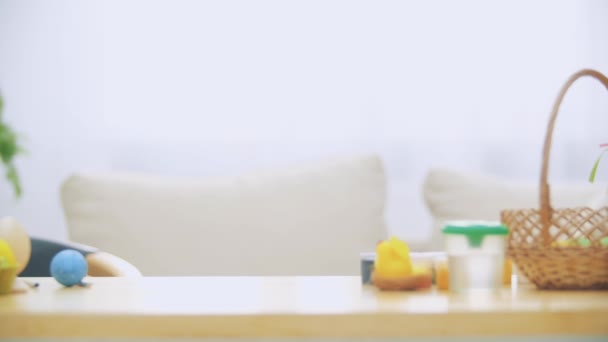 Pequeño niño jugando con orejas de conejo en la cabeza se esconde debajo de la mesa de madera, llena de decoraciones de Pascua. Chico está jugando con conejitos de Pascua en la mesa, escondiendo su cara . — Vídeos de Stock