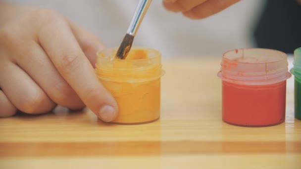 Creative boy is mixing and stirring yellow paint in a jar with a help of nude paint-brush. — Stock Video