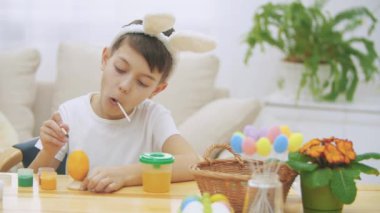 Bir Paskalya yumurta sarı renkte bir colourizing, masada oturmuş ve turuncu bir lolipop tatma Intersted ve konsantre çocuk bitti.