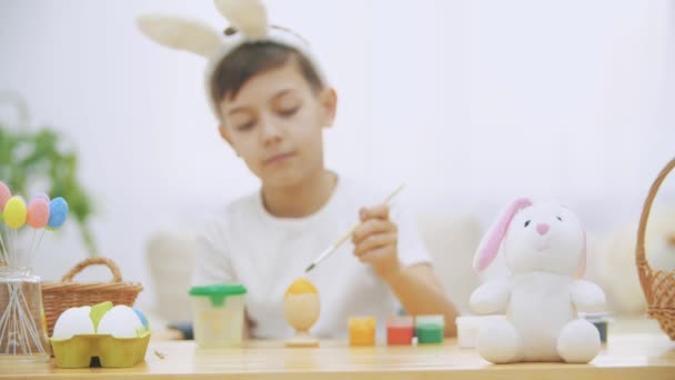 Креативный мальчик раскрашивает пасхальное яйцо в желтый цвет с помощью кисти . — стоковое видео