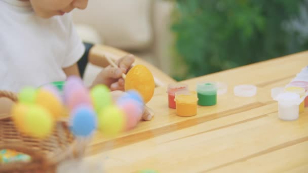 Інтерстед і концентрований хлопчик закінчують фарбувати пасхальне яйце жовтого кольору, сидячи за столом . — стокове відео