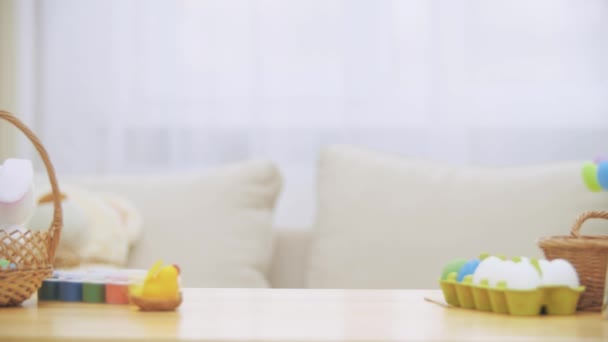 Pequeña niña jugando con orejas de conejo en la cabeza se esconde debajo de la mesa de madera, llena de decoraciones de Pascua. Chica está jugando con un conejo blanco de Pascua en la mesa, slolwly mostrando su encantadora cara — Vídeos de Stock