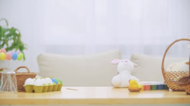 Linda niña con orejas de conejo se esconde debajo de la mesa llena de decoraciones de Pascua. Pequeño conejito blanco lindo está atacando chica amablemente. Laught es la habitación . — Vídeos de Stock