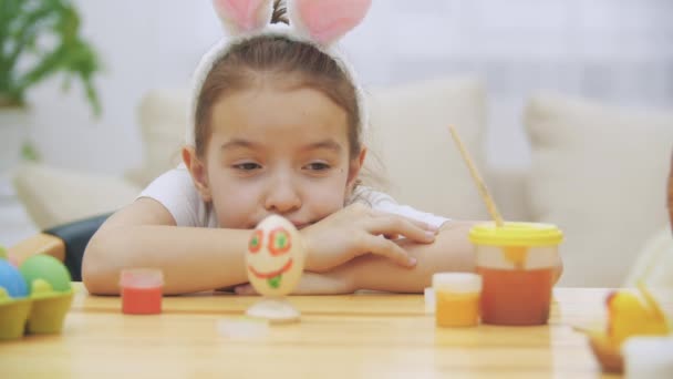 Cansado linda chica está acostado en la mesa y mirando a su creación. Huevo de Pascua divertido coloreado . — Vídeo de stock