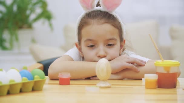 疲れているかわいい女の子はテーブル横になって、彼女の作成を見てします。突然、復活祭の卵以上の女の子になり、我々 はどのように彼女はそれを colourized が参照してください。. — ストック動画