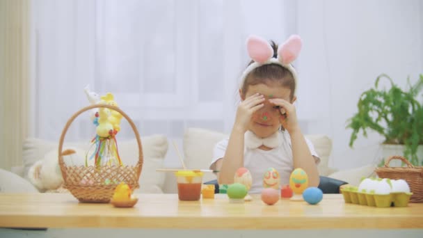 Pequeña linda chica con orejas de conejo está escondiendo su hermosa cara. Repentinamente muestra su cara coloreada en colores brillantes y sonriendo ampliamente, mostrando sus dientes . — Vídeo de stock