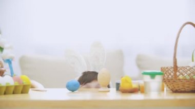 Küçük oyun çocuk w ahşap masanın altından Paskalya süsleri tam saklıyor. Çocuk göz kırpıyor ve gözleri ile gülümseyen yüzünü gizleme.