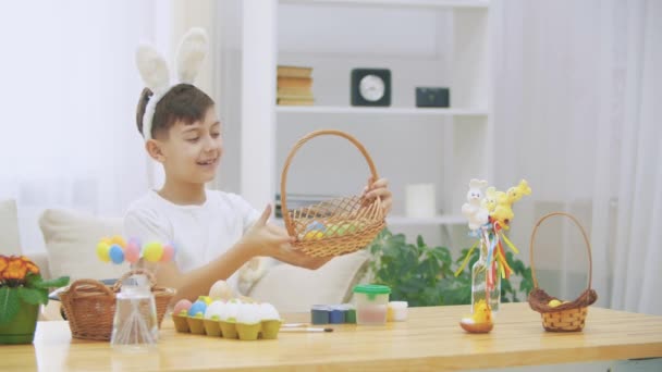 Der kleine, fröhliche Junge nimmt einen hölzernen Korb und zeigt, wie viele bunte Ostereier es gibt, und hebt den Daumen verdreht nach oben.. — Stockvideo