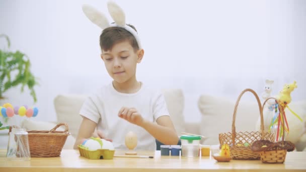 Menino bonito e adorável está sorrindo e colorindo galinhas ovo e mostrando dois, que já foram coloridos em rosa e amarelo, em suas mãos. Conceito feriado de Páscoa . — Vídeo de Stock