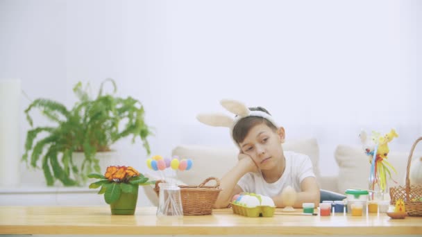 かわいいすてきな男の子はテーブルに座っている疲れ、休息することを決めた。少年はあくびです。最後に彼は面白いウサギの通知、それらを果たしています。遊び心のある少年. — ストック動画