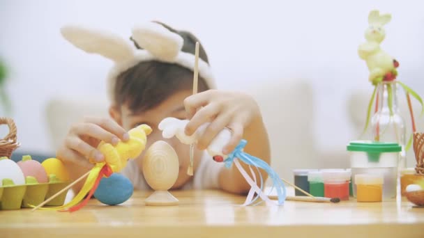 Jeune garçon adorable est assis à la table pleine de décorations de Pâques et joue avec des lapins de Pâques dans ses mains. Discussion de lapins. Qui peindrait un théâtre Bunny oeuf . — Video