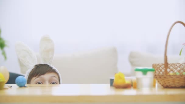 Schattige jongen is verbergen onder de tafel vol met Pasen decoraties en speelt met de paashaas in zijn hand. Bunny theater. Discussie. Gesprek: vrolijke jongen en een zachte konijn. — Stockvideo