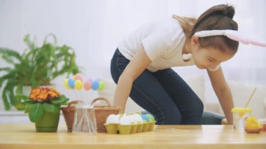 Küçük güzel kızın yumuşak bir koltuğa tırmanma ve bunny ile oynuyor. O Paskalya süsleri ile masada oturur ve bir tavşan boyama.