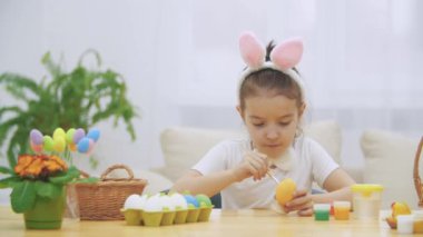 Küçük oynak kız, tavşan kulakları kafasında giymiş seçerek bir kırmızı bir yumurta boyamak için renk ve sakince bir Paskalya yumurta boyama.