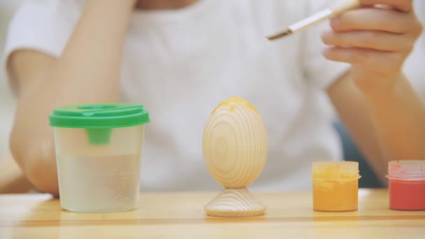 Kreativa pojke målar ett påskägg i en gul färg med hjälp av pensel. — Stockvideo
