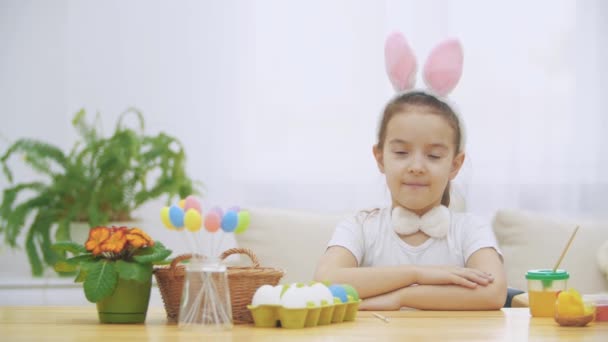 Piccola ragazza carina e adorabile sorride sinceramente. Prende un uovo di Pasqua dal cesto e lo guarda. Ragazza sta salutando con il suo liitle piatto di mano. Concetto vacanza di Pasqua . — Video Stock