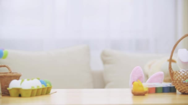 Pequeña niña jugando con orejas de conejo en la cabeza se esconde debajo de la mesa de madera, llena de decoraciones de Pascua. Chica está jugando mostrando slolwly su encantadora cara . — Vídeos de Stock