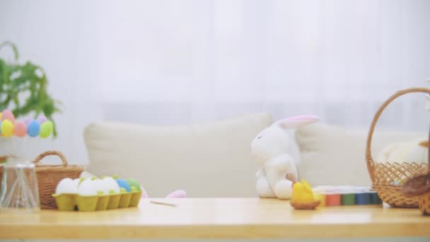 Urocza dziewczyna ukrywa pod stół pełen ozdoby wielkanocne i bawi się z Easter bunny w ręku. — Wideo stockowe