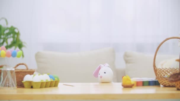 Joven chica adorable se esconde debajo de la mesa llena de decoraciones de Pascua y está jugando con el conejo de Pascua en su mano. Bunny invita a la chica a se un mundo maravilloso . — Vídeos de Stock