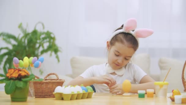 Menina brincalhão, usando orelhas de coelho em sua cabeça está escolhendo uma cor vermelha para pintar um ovo . — Vídeo de Stock