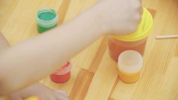 Menina criativa escolheu vermelho para pintar. Menina encantadora está desenhando vermelho perto de um sorriso verde no ovo de Páscoa. Conceito de Páscoa, mesa decorada com uma variedade de cores de primavera . — Vídeo de Stock