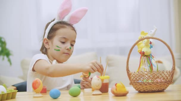 素敵なかわいい女の子楽しい復活祭の卵の絵があります。愛らしい少女エステル卵の色分けです。少女の美しさと彼女の顔にスポットし、猫ウィスカー、木製のテーブルに座って優しく微笑む、 — ストック動画