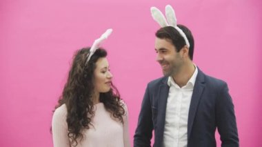 Genç pembe bir arka plan üzerinde ayakta duran çift. Bu süre boyunca, onlar ayaktakımı kulaklarında giyindin. Birbirimizi, konuşma ve gülümseme arıyorum.
