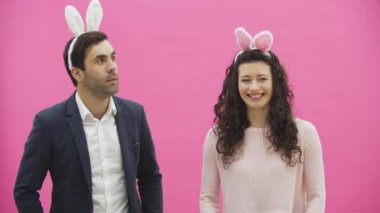 Genç pembe bir arka plan üzerinde ayakta duran çift. Bu süre boyunca, onlar ayaktakımı kulaklarında giyindin. Birbirine bakarak gülümser içtenlikle