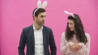 Pembe bir arka plan üzerinde duran genç güzel çift. Bunlar olurken, onlar ayaktakımı kulaklarında giyindin. Yavaşça birbirine, aşık bakarak.