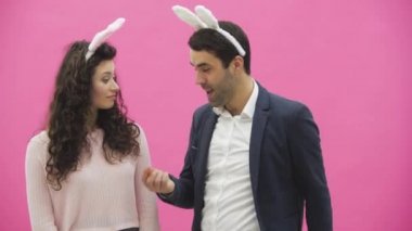 Genç çift, pembe arka plan güzel. Bu süre boyunca, onlar ayaktakımı kulaklarında giyindin. Birbirine bakarak. Bir adam havuç gösterir ve eşi gülmeye başlar. Genç bir adam boğmaya başlar