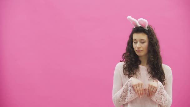 Jonge mooie paar staande op een roze achtergrond. Ze maken tijdens deze bewegingen van konijnen. De vrouw legde haar handen op haar nek. Zachte weergaven en raakt met elkaar zijn verbonden. Op de hoofd oren van het konijn. — Stockvideo