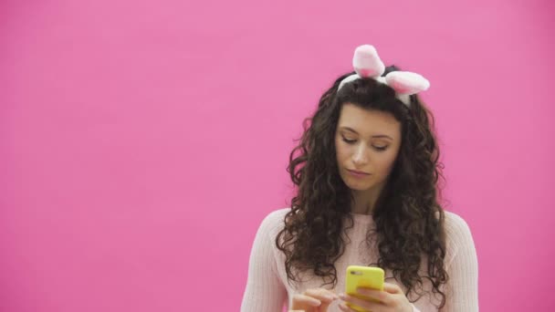 Mooi jong meisje staande op een roze achtergrond. Tijdens dit zijn er oren van konijnen op het hoofd. — Stockvideo