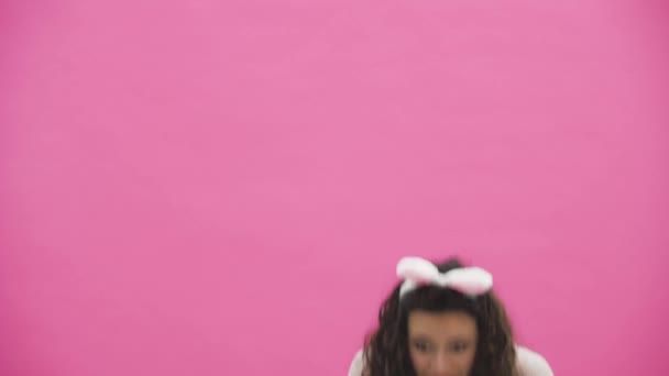 schöne junge Mädchen steht auf einem rosa Hintergrund. Dabei gibt es Hasenohren auf dem Kopf.