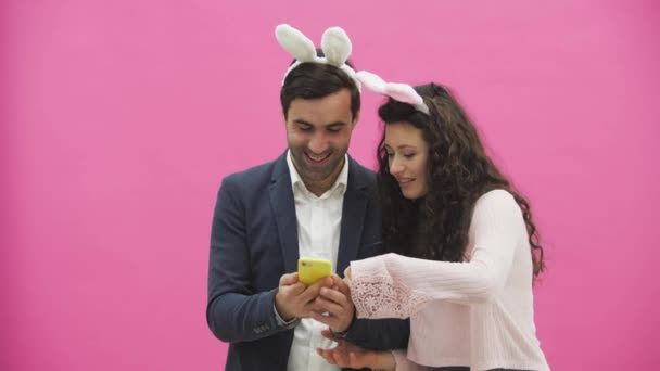 Giovani amanti coppia su sfondo rosa. Con orecchie rabbiose sulla testa. Durante questa foto di Pasqua, sephi fare al telefono e guardarli gioire . — Video Stock