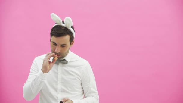 Beautiful boy standing on a pink background. During this dressed in a white shirt. Holding a carrot wants to burn it like a cigar. After a while, he throws carrots to the ground. — Stock Video