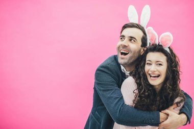 Pembe bir arka plan üzerinde duran genç mutlu çift. Kafasına bir kanca ile. Karısı sarılma, adam tarafına benziyor. İçtenlikle gülümse. Paskalya.