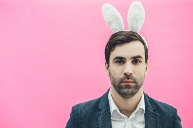Pembe bir arka plan üzerinde genç adam. Uzun tavşan kulakları giyinmiş bir adam. Bu yakın çekim sırasında kameraya bakıyor. Bir ceket giymiş ve çok ciddi. Paskalya.
