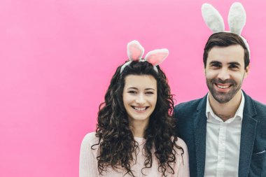 Genç çift ayakta pembe bir arka plan üzerinde güzel. Aynı zamanda eşi yanında duruyor. İçtenlikle gülümse ve kafanı çevir. Paskalya kavramı.