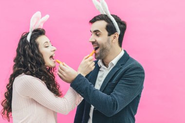 Pembe bir arka plan üzerinde duran genç mutlu çift. Tavşan kulakları kafasına. Bu sırada adam ve karısı elinde küçük havuç ağızları açık tutarak birbirine besleme. İçtenlikle gülümse