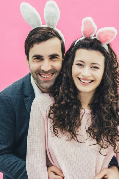 Junges, energisches Paar auf rosa Hintergrund. mit Hasenohren auf dem Kopf. glücklich und verliebt lächeln aufrichtig in die Kamera der. Ostern. — Stockfoto