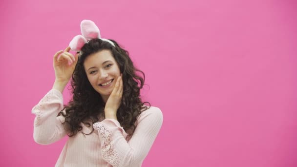 Святковий Великодній святковий сезон. Усміхнена молода жінка у великодніх вухах кролика на рожевому фоні стрибає і дивиться на простір для копіювання . — стокове відео